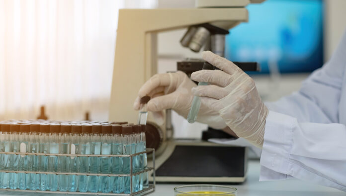 Biochemistry laboratory research, Chemist is analyzing sample in laboratory with Microscope equipment and science experiments glassware containing chemical liquid.